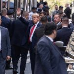 Donald Trump waving while surrounded by security personnel on a city street