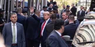 Donald Trump waving while surrounded by security personnel on a city street