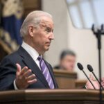 Joe Biden speaking at a podium with hands raised