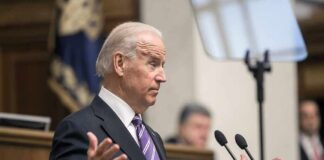 Joe Biden speaking at a podium with hands raised