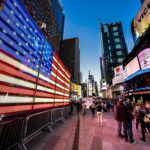 American flag LED display in a busy city square at dusk
