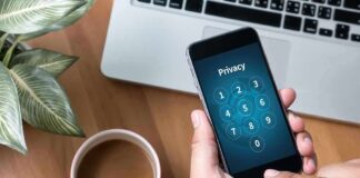 Hands holding smartphone with passcode screen near laptop and coffee