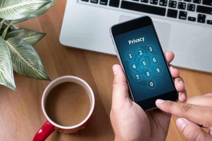 shutterstock_489314119 Hands holding smartphone with passcode screen near laptop and coffee