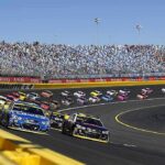 Stock cars racing on a banked track with grandstands in background