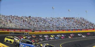 Stock cars racing on a banked track with grandstands in background
