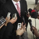 Man in suit surrounded by microphones and recorders