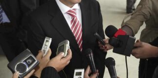 Man in suit surrounded by microphones and recorders