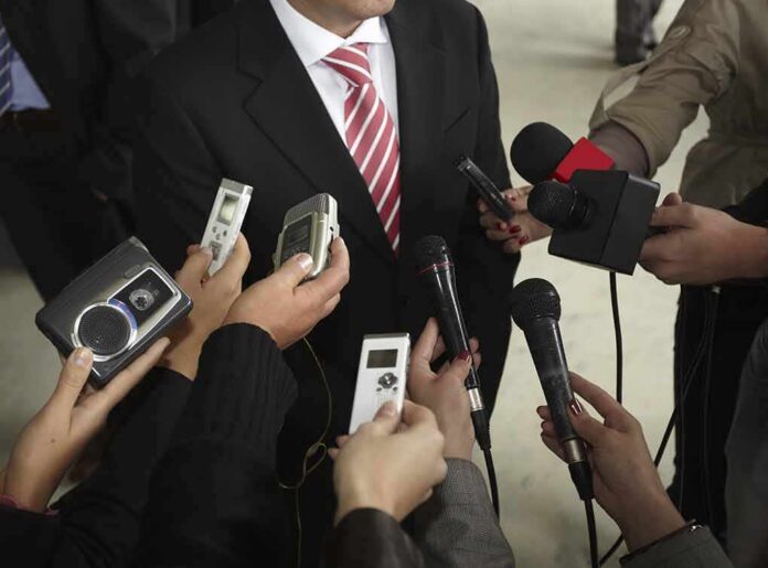 Man in suit surrounded by microphones and recorders