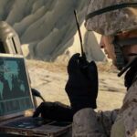 soldier using a rugged laptop and radio in a desert setting