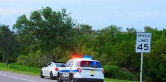 Police SUV with lights on behind a white car on roadside near 45 mph sign