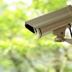 A security camera mounted outdoors with a blurred green background
