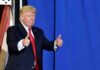 Donald Trump giving two thumbs up in front of a blue curtain