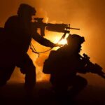 Two armed soldiers silhouetted against fiery smoke