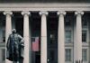 Statue in front of a neoclassical government building with columns and a U.S. flag
