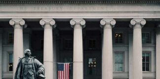 Statue in front of a neoclassical government building with columns and a U.S. flag