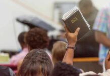 Churchgoers Targeted – Dem Elites’ Quiet Contempt? Hand holding a Bible in a crowded church service