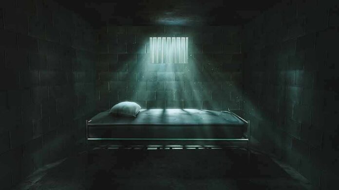 Prison cell with single metal bed under barred window