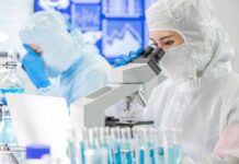Scientist in protective suit using a microscope