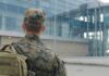 soldier in camouflage with backpack outside modern glass building