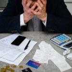 Stressed person with head in hands at a desk with bills and calculator