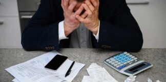 Stressed person with head in hands at a desk with bills and calculator