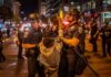 Radical Chants, Shattered Glass – Then Police Charge Police officers detain a protester at night on a city street