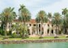 Waterfront mansion with palm trees and grand columns