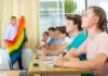 Students in classroom listening as teacher holds rainbow flag