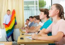 Students in classroom listening as teacher holds rainbow flag