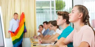 Students in classroom listening as teacher holds rainbow flag