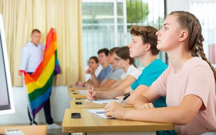 Students in classroom listening as teacher holds rainbow flag