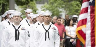 Dontrelle Inman and Anthony C. Ferrante among U.S. Navy sailors at a ceremony with an American flag